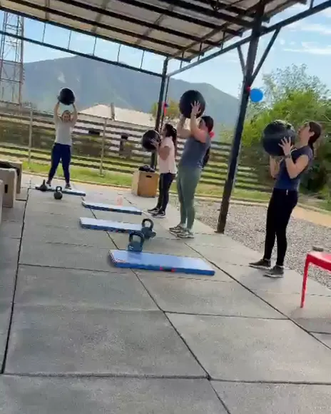 Alumnas lanzando balones medicinales bajo el techo del box, con los cerros de fondo