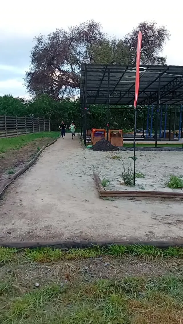 Sendero de tierra del parque que lleva al galpón techado del box, con dos personas trotando
