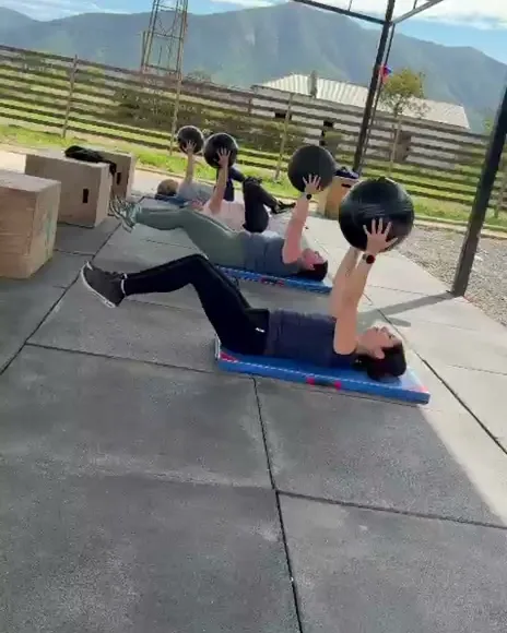 Alumnas haciendo abdominales con balón medicinal sobre colchonetas, bajo el techo del box