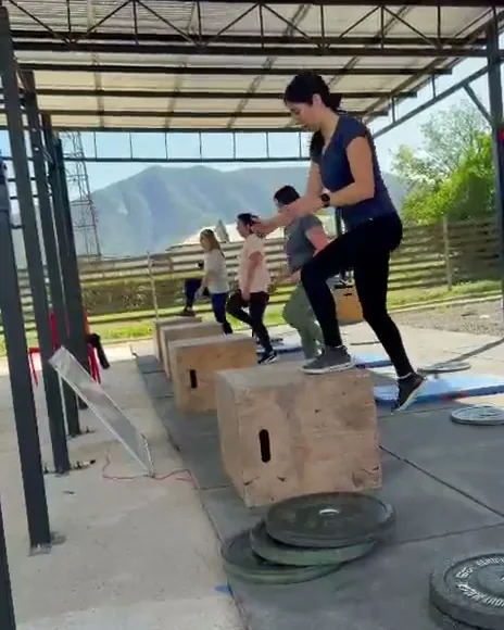 Alumna subiendo a un cajón de madera junto a discos apilados, con el grupo detrás